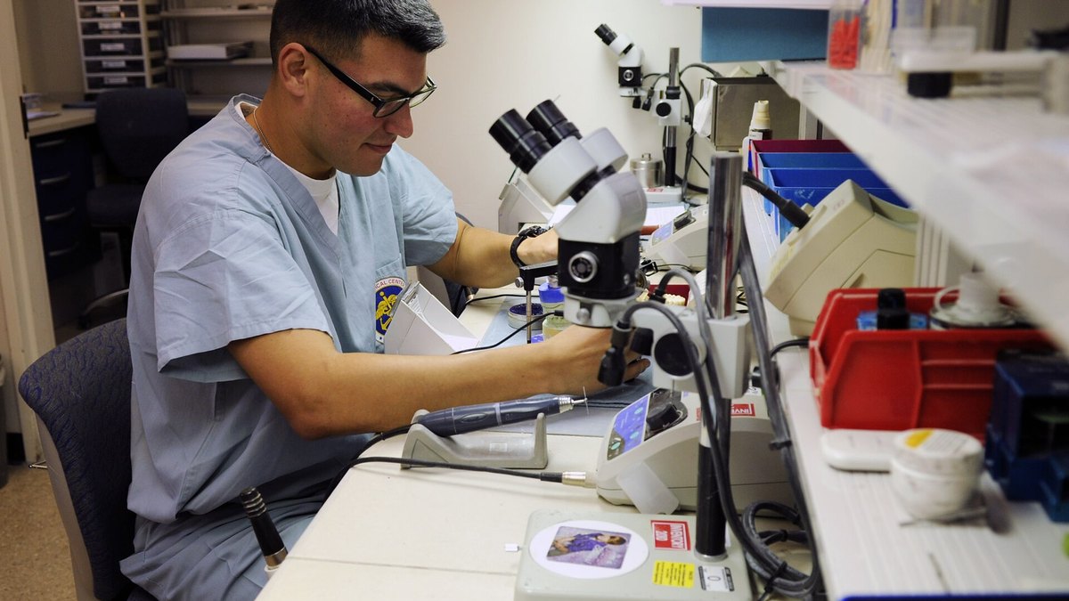 A dental technician hand-shaping a replacement tooth in the laboratory, the mechanical craft that tooth regeneration aims to turn into a biological process — a Panacea Bio Chem reference by Bogdan Dicoias